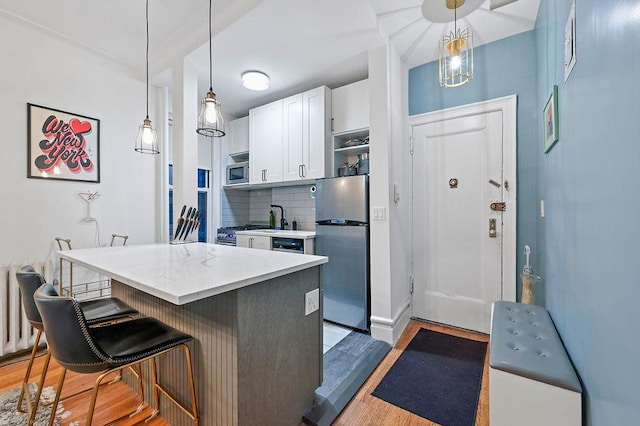 kitchen featuring stainless steel appliances, a kitchen breakfast bar, white cabinets, light wood-type flooring, and decorative backsplash