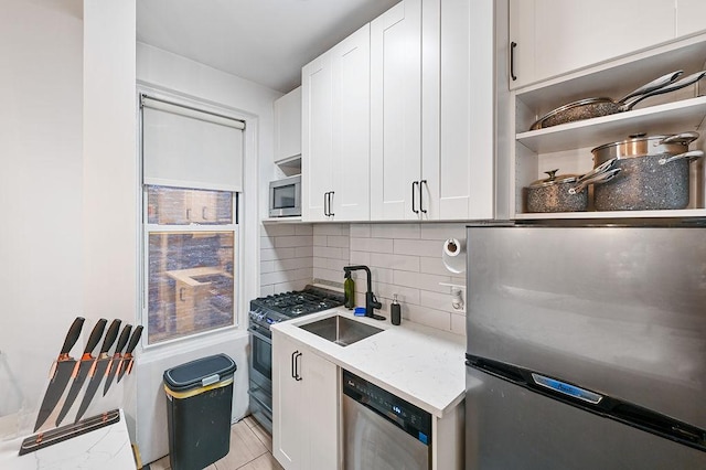 kitchen with light stone counters, stainless steel appliances, decorative backsplash, white cabinetry, and a sink