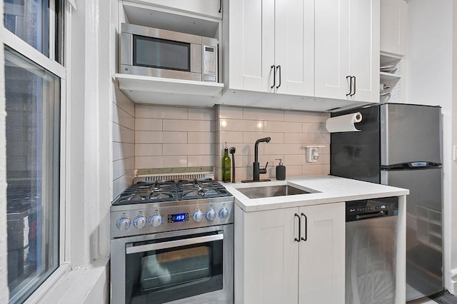 kitchen featuring appliances with stainless steel finishes, white cabinets, a sink, and tasteful backsplash