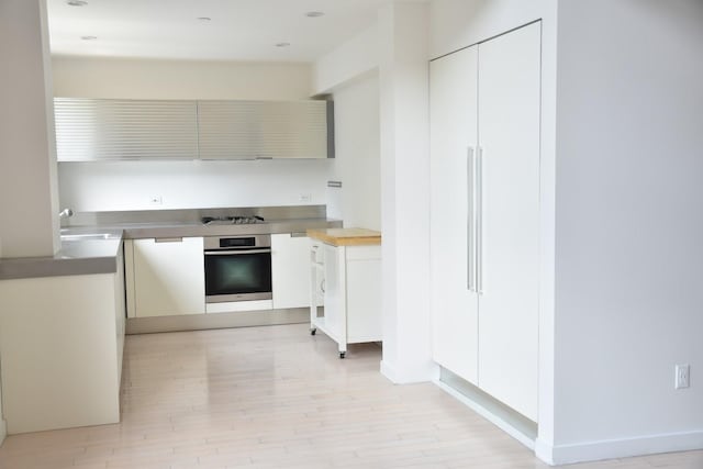 kitchen with gas stovetop, light wood-style flooring, stainless steel oven, and a sink