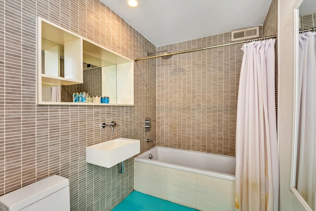 full bathroom featuring toilet, a sink, tiled shower / bath, and tile walls