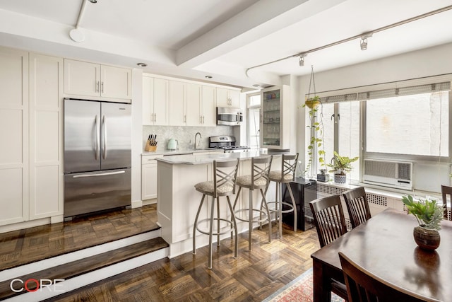 kitchen featuring appliances with stainless steel finishes, a kitchen bar, backsplash, and white cabinets