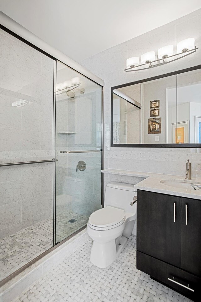 bathroom featuring a shower stall, toilet, vanity, and tile walls