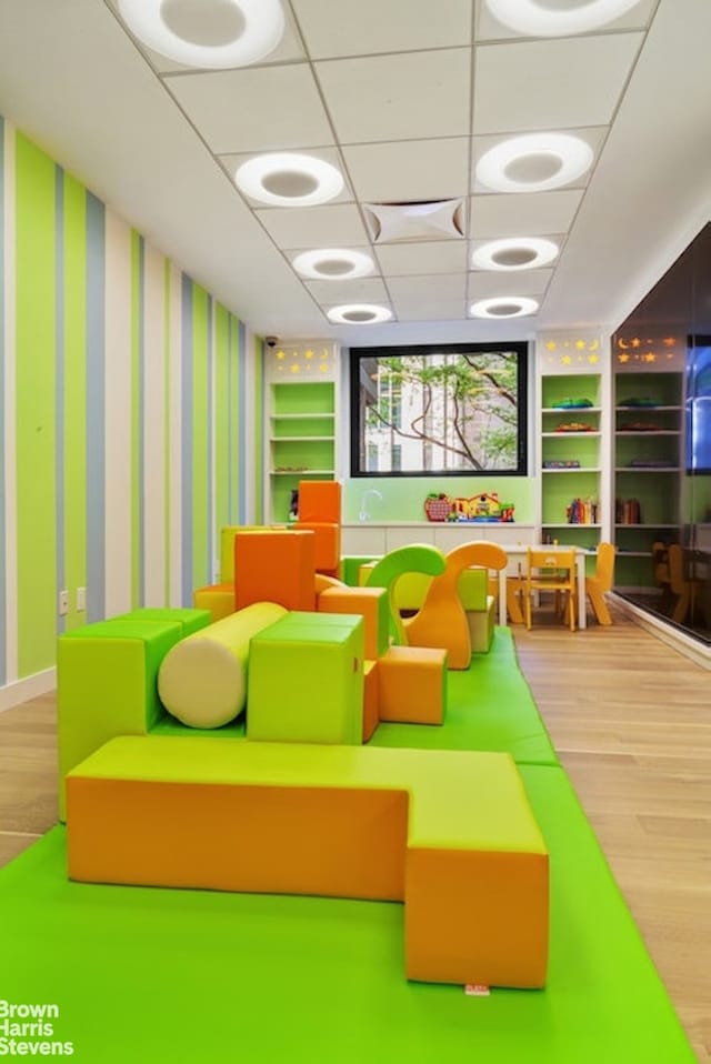 recreation room with wallpapered walls, built in shelves, a drop ceiling, and wood finished floors