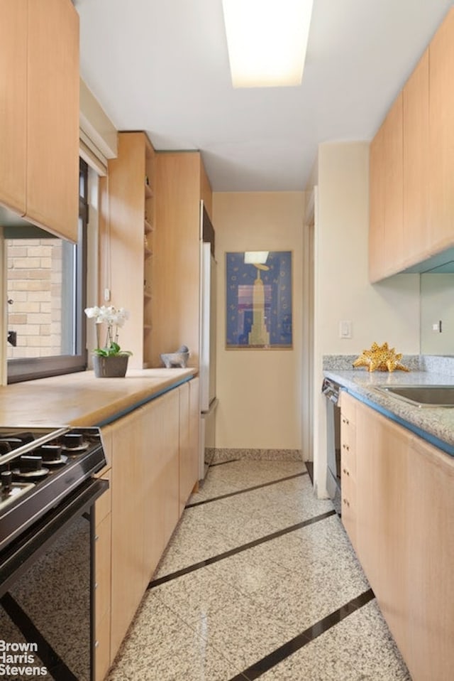 kitchen featuring light countertops, light brown cabinetry, gas range, fridge, and baseboards
