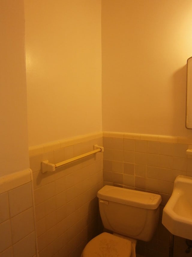 half bath featuring a wainscoted wall, a sink, toilet, and tile walls