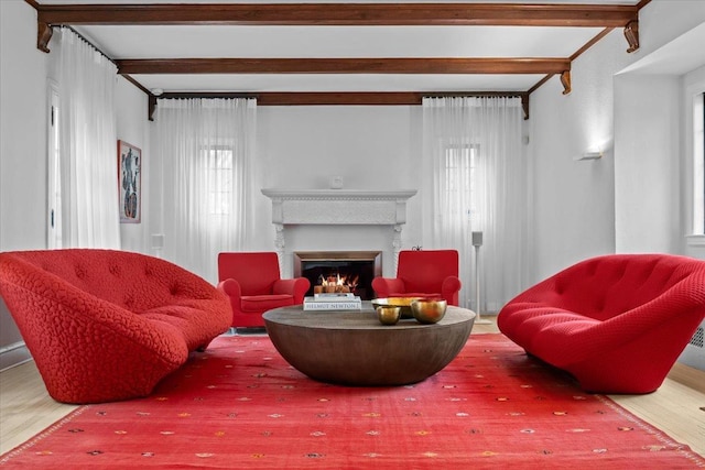 living room with a warm lit fireplace, beamed ceiling, and wood finished floors