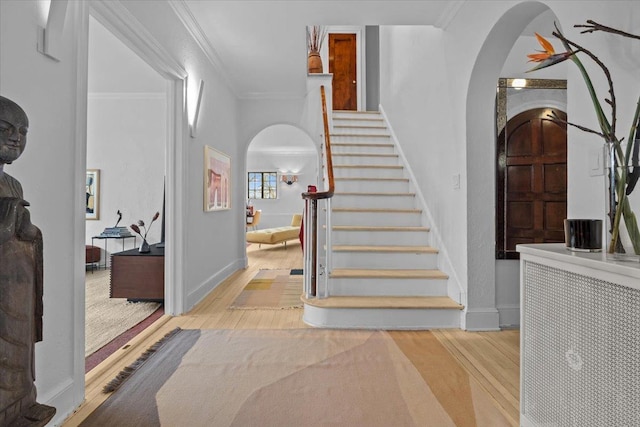 foyer entrance with arched walkways, crown molding, wood finished floors, baseboards, and stairs