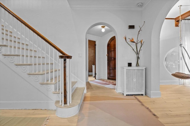 foyer featuring ornamental molding, arched walkways, baseboards, and wood finished floors