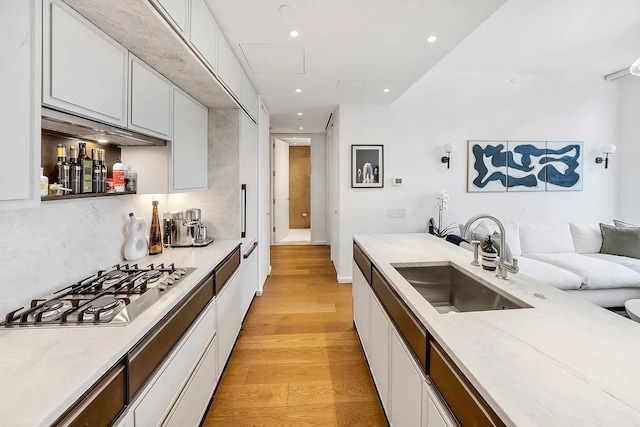 kitchen featuring a sink, white cabinets, light countertops, light wood finished floors, and stainless steel gas stovetop