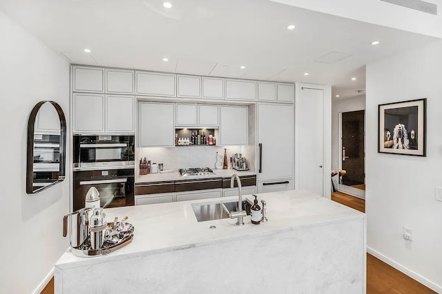 kitchen featuring baseboards, wood finished floors, a sink, backsplash, and recessed lighting