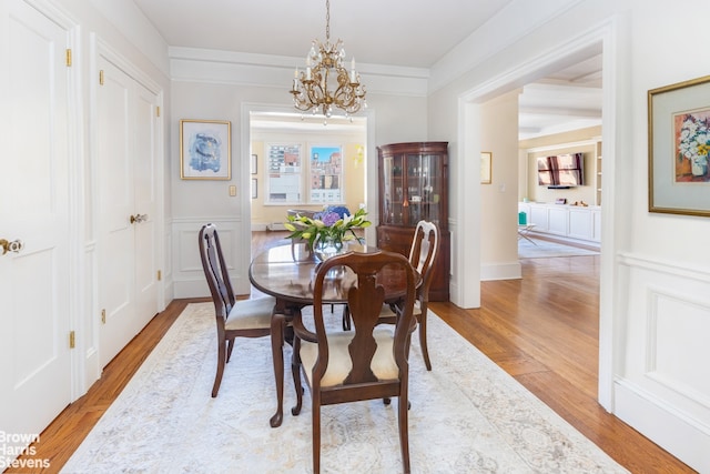 dining space with built in features, wainscoting, an inviting chandelier, light wood-style floors, and a decorative wall