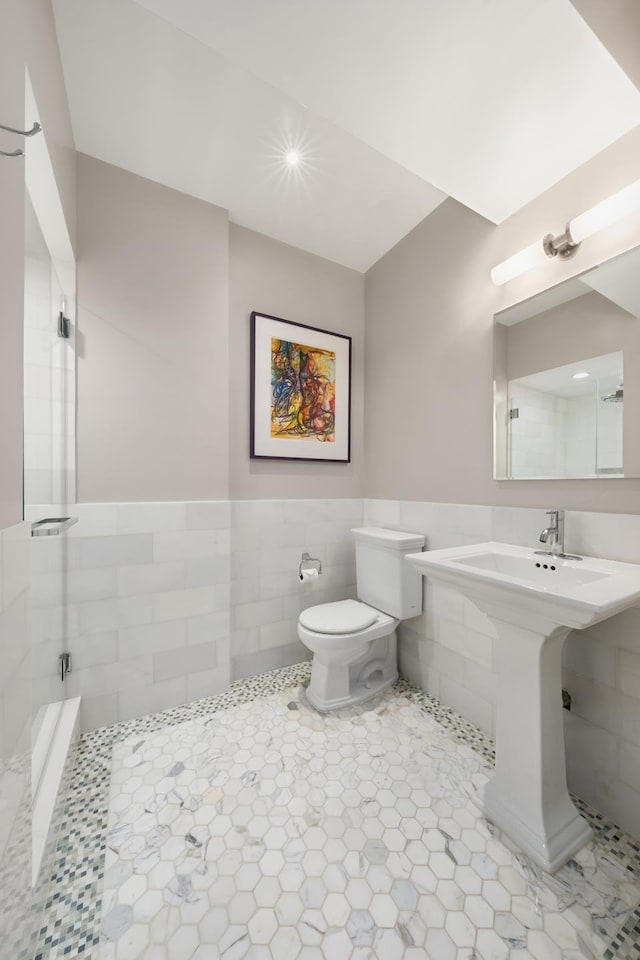 bathroom with toilet, tile walls, tiled shower, wainscoting, and tile patterned floors