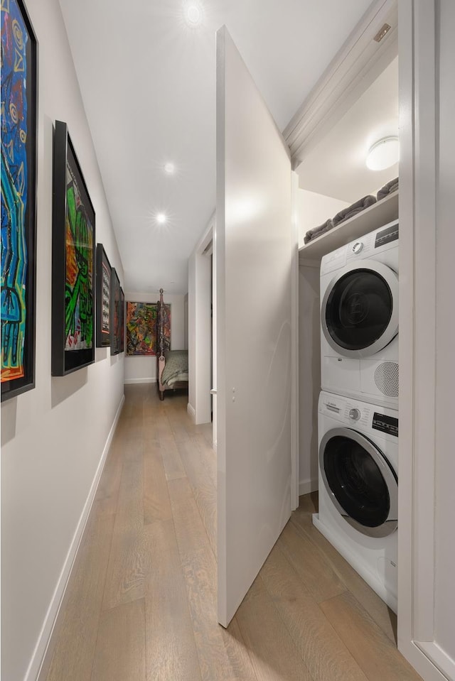 washroom featuring stacked washer and dryer, laundry area, baseboards, and light wood finished floors