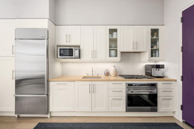 kitchen featuring light countertops, decorative backsplash, white cabinetry, a sink, and built in appliances