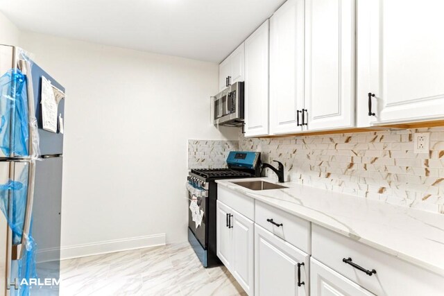 kitchen featuring stainless steel appliances, a sink, white cabinetry, backsplash, and light stone countertops