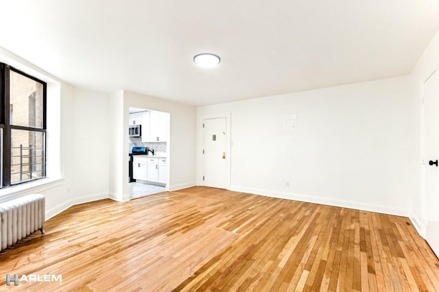 unfurnished room with radiator heating unit, light wood-style flooring, and baseboards