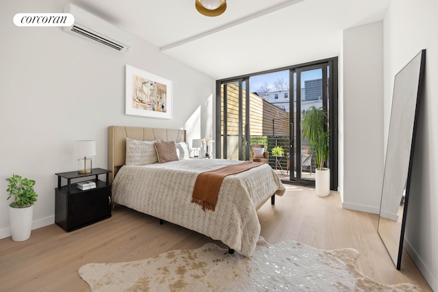 bedroom featuring a wall mounted air conditioner, light wood-type flooring, expansive windows, baseboards, and access to exterior