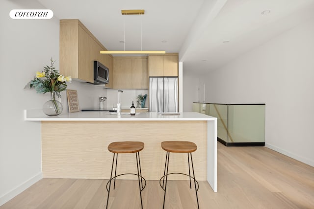 kitchen featuring light wood finished floors, light brown cabinetry, a kitchen bar, a peninsula, and stainless steel appliances