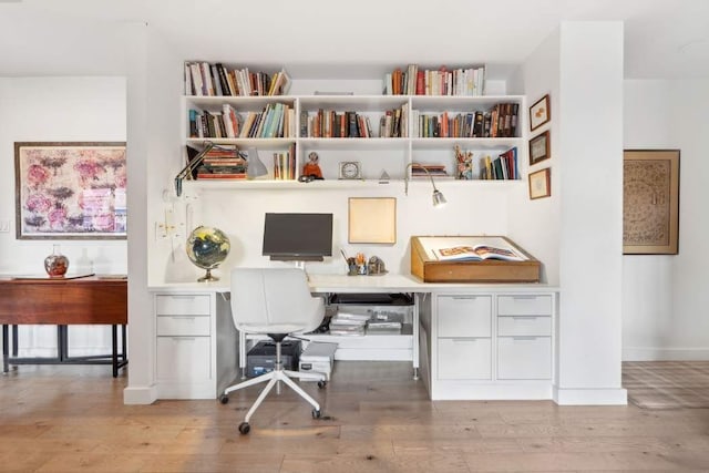 home office with built in study area, baseboards, and wood finished floors