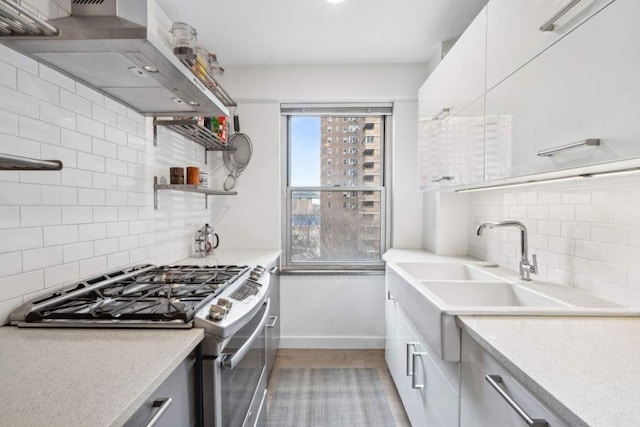 kitchen with stainless steel range with gas cooktop, wall chimney exhaust hood, open shelves, tasteful backsplash, and baseboards