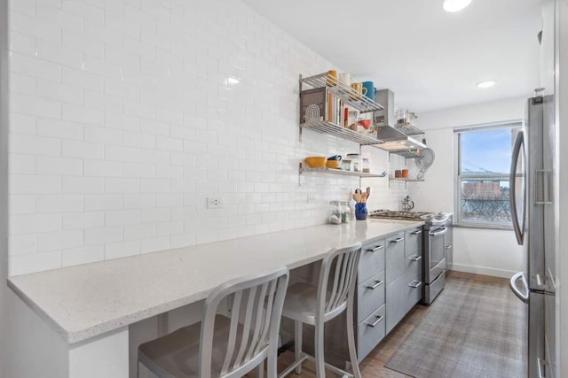 kitchen with light stone counters, built in desk, open shelves, tasteful backsplash, and appliances with stainless steel finishes