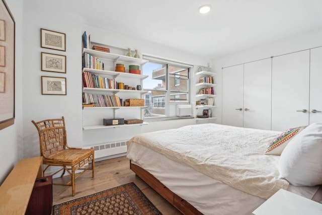 bedroom with a closet, recessed lighting, wood finished floors, and radiator