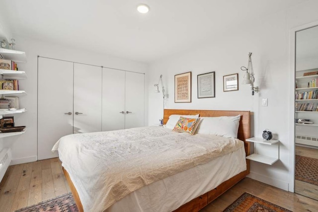 bedroom with a closet, radiator, wood-type flooring, and baseboards