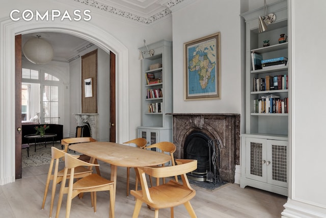 dining space featuring light wood-type flooring, built in shelves, ornamental molding, and a fireplace