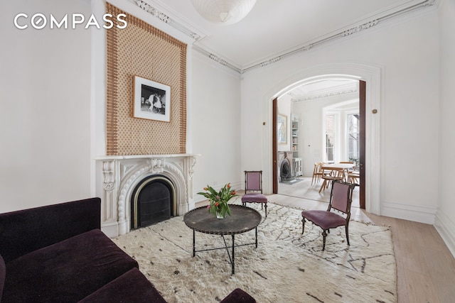 living room with wood finished floors, baseboards, a fireplace, arched walkways, and ornamental molding