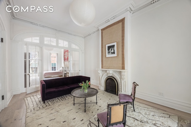 living room featuring a fireplace, crown molding, baseboards, and wood finished floors