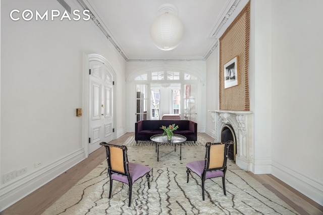 living area featuring a high end fireplace, crown molding, baseboards, and wood finished floors