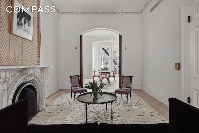 sitting room with arched walkways, a fireplace, crown molding, and light wood-style floors