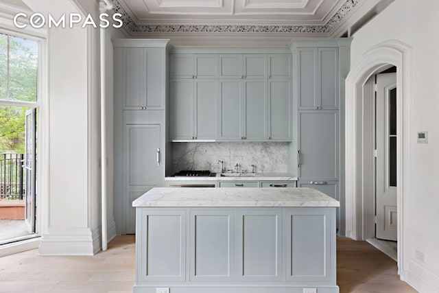 kitchen with light wood finished floors, backsplash, a kitchen island, ornamental molding, and light stone counters