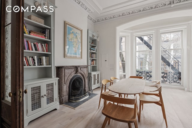 dining room featuring light wood-style flooring, a fireplace, a raised ceiling, and ornamental molding