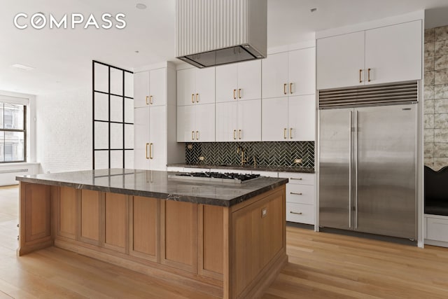 kitchen featuring gas stovetop, stainless steel built in fridge, decorative backsplash, light wood-type flooring, and a center island