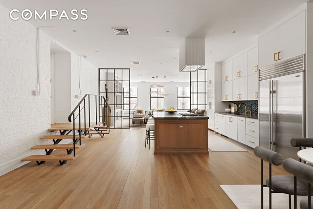 kitchen with visible vents, light wood finished floors, stainless steel built in fridge, dark countertops, and a center island