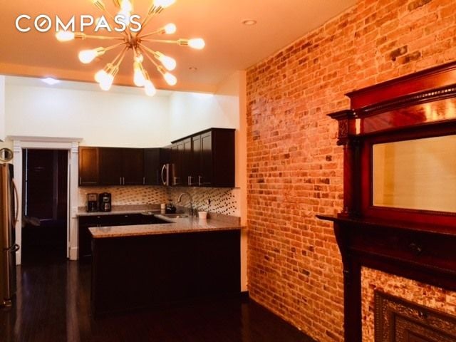 kitchen with a sink, an inviting chandelier, a peninsula, brick wall, and decorative backsplash