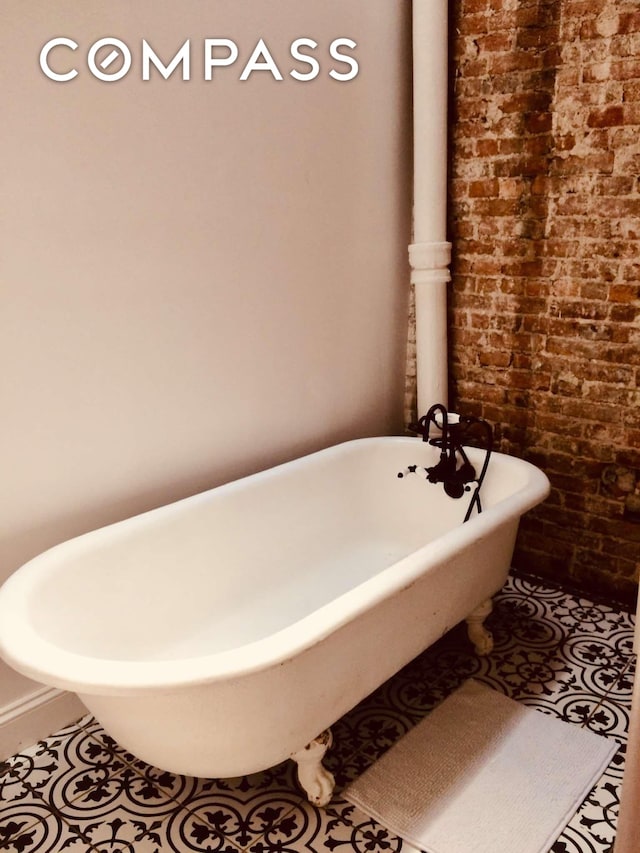 bathroom with tile patterned floors, brick wall, and a freestanding bath