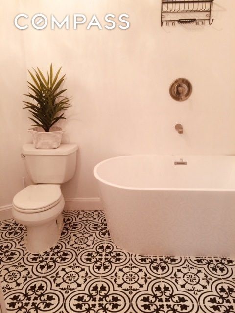 full bath featuring a freestanding tub, baseboards, toilet, and tile patterned flooring