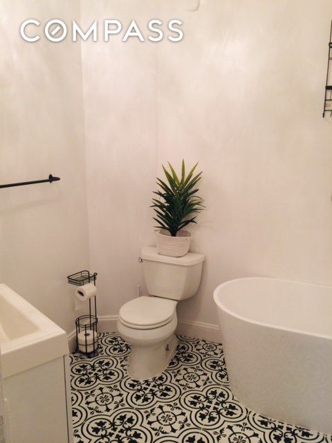 full bath featuring tile patterned floors, toilet, a tub to relax in, and baseboards