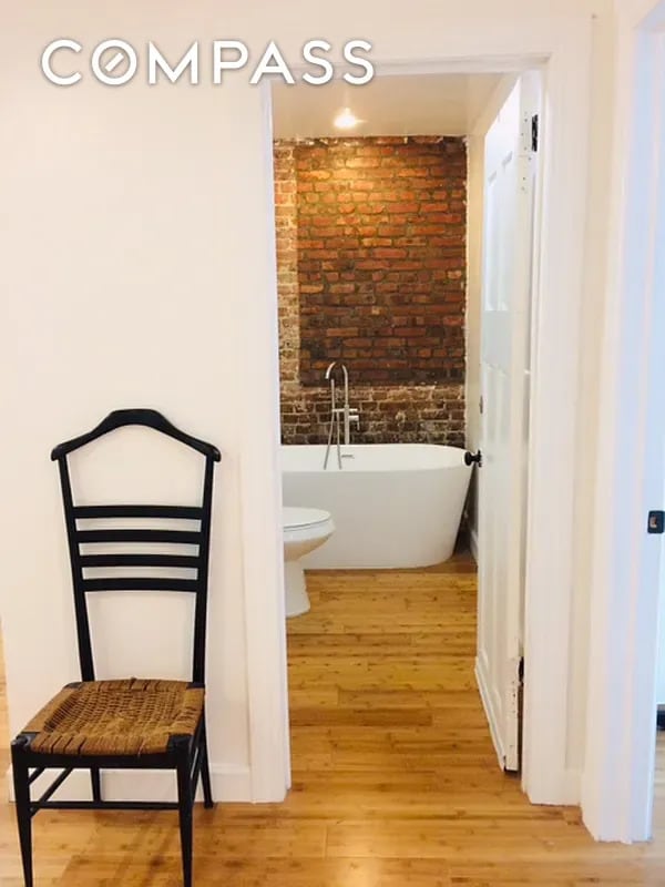 full bath with a soaking tub, wood finished floors, and brick wall