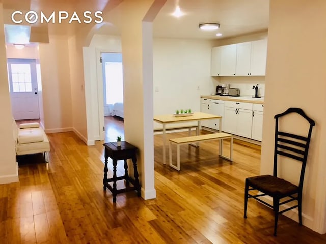 interior space with baseboards, arched walkways, light countertops, wood-type flooring, and white cabinetry