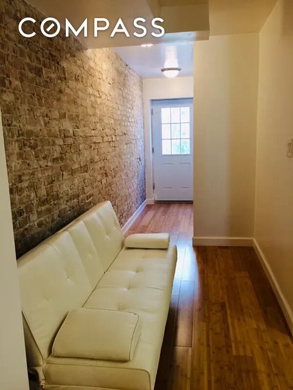 doorway to outside with wood finished floors, baseboards, and brick wall