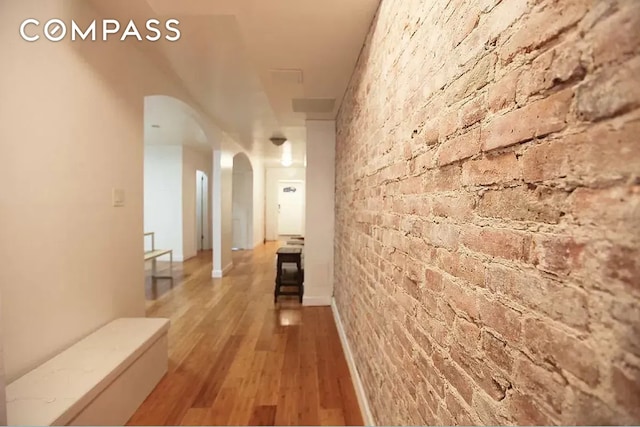 hall featuring wood finished floors, arched walkways, and brick wall