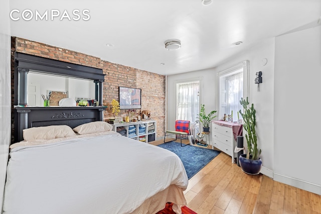 bedroom with baseboards, brick wall, and hardwood / wood-style flooring