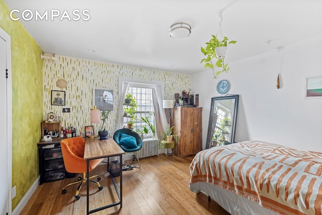 bedroom with wallpapered walls, hardwood / wood-style flooring, radiator heating unit, and baseboards