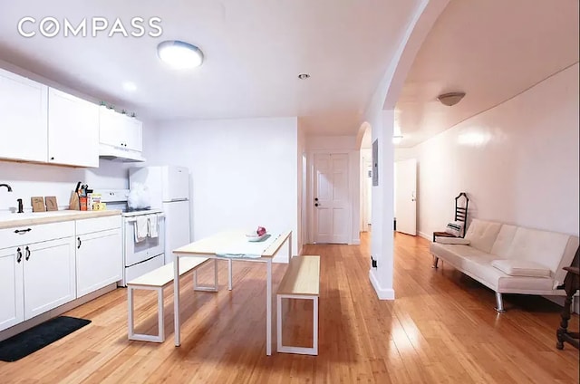 kitchen with arched walkways, light wood-style flooring, white appliances, and white cabinetry