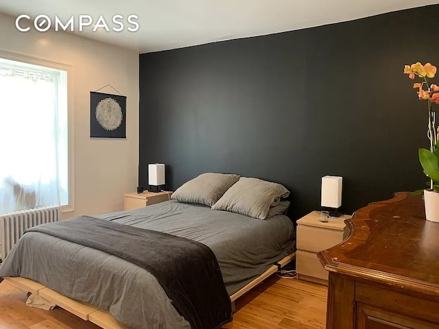 bedroom featuring multiple windows, radiator, and light wood-style flooring