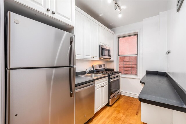 kitchen with light wood finished floors, dark countertops, appliances with stainless steel finishes, white cabinetry, and a sink